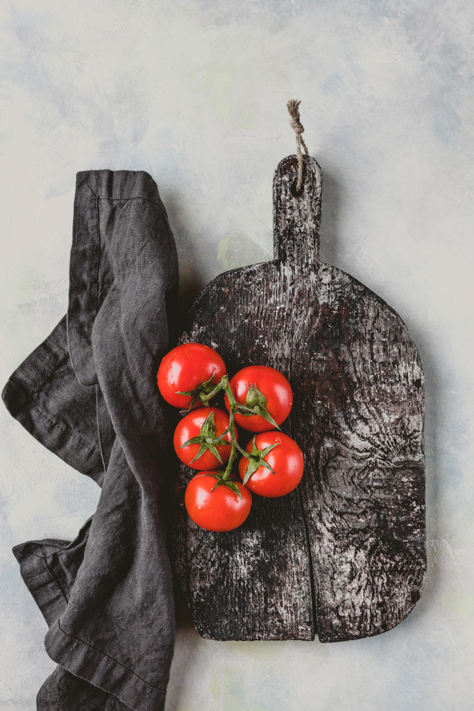 top view of kitchen towel, cutting board and cherry tomatoes on marble table  - Photo, Image