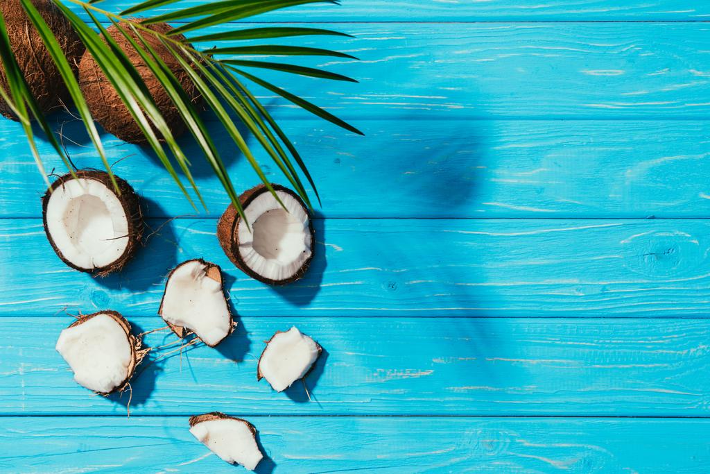 вид сверху на кокосы и зеленые пальмовые листья на бирюзовой деревянной поверхности
 - Фото, изображение