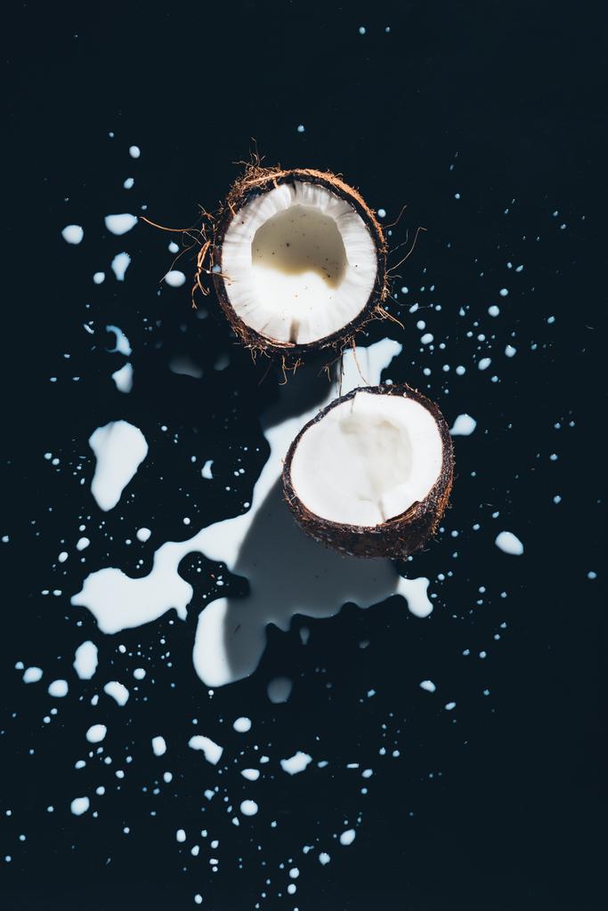 bovenaanzicht van gehalveerde biologische kokosnoot en de kokosmelk op zwart - Foto, afbeelding