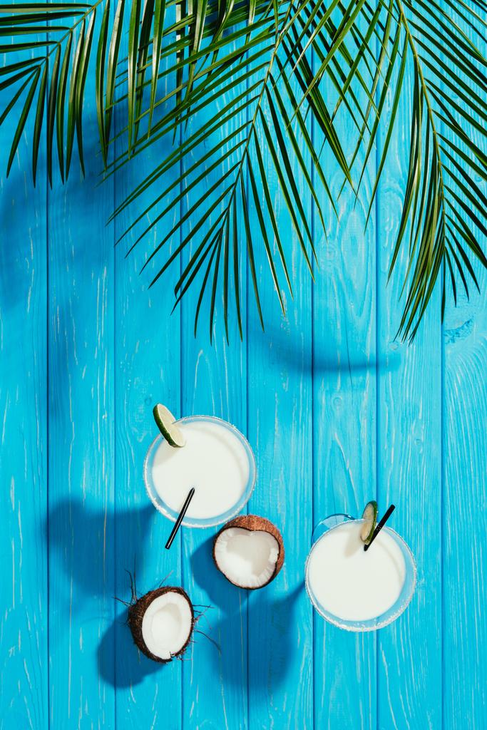 bovenaanzicht van kokosnoot cocktails in glazen en gebarsten kokosnoot op blauwe tafelblad - Foto, afbeelding