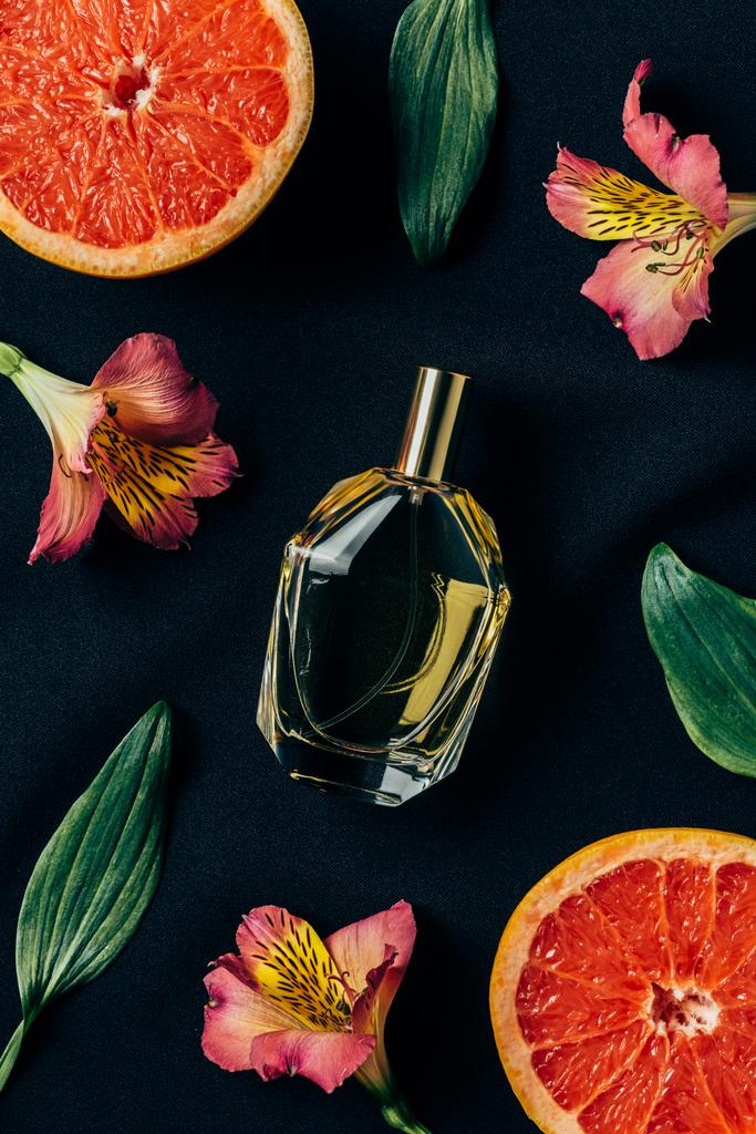 верхний вид бутылки духов окруженный цветами альстромерии и ломтиками грейпфрута на черном
 - Фото, изображение