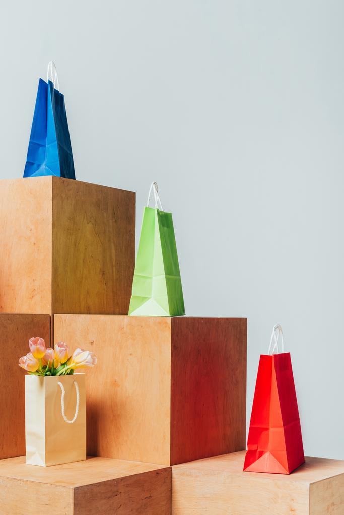 barevné papírové tašky a tulipány na dřevěných stánků izolované na bílém, letní prodejní koncept - Fotografie, Obrázek