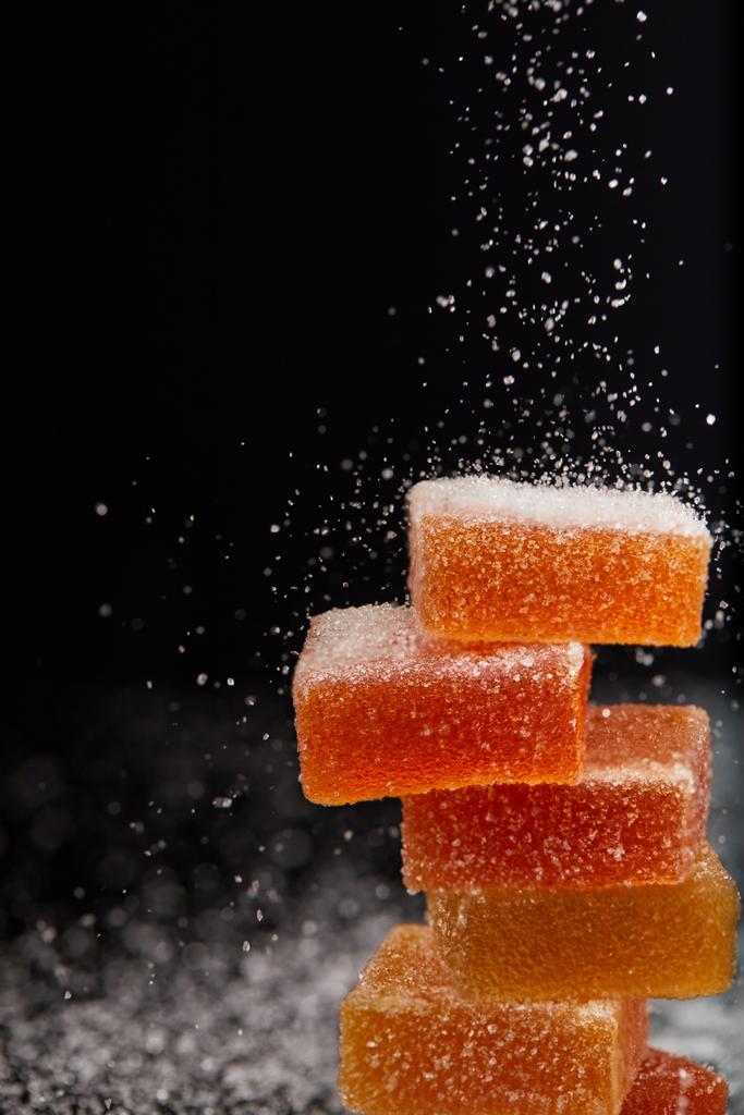 Close-up shot van suiker die over jelly snoepjes op zwarte achtergrond  - Foto, afbeelding