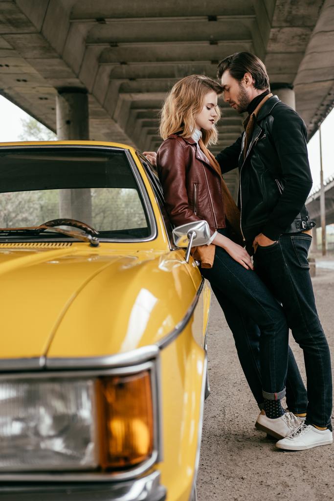vista lateral de hermosa pareja joven sensual abrazándose mientras se inclina en el coche amarillo
 - Foto, Imagen