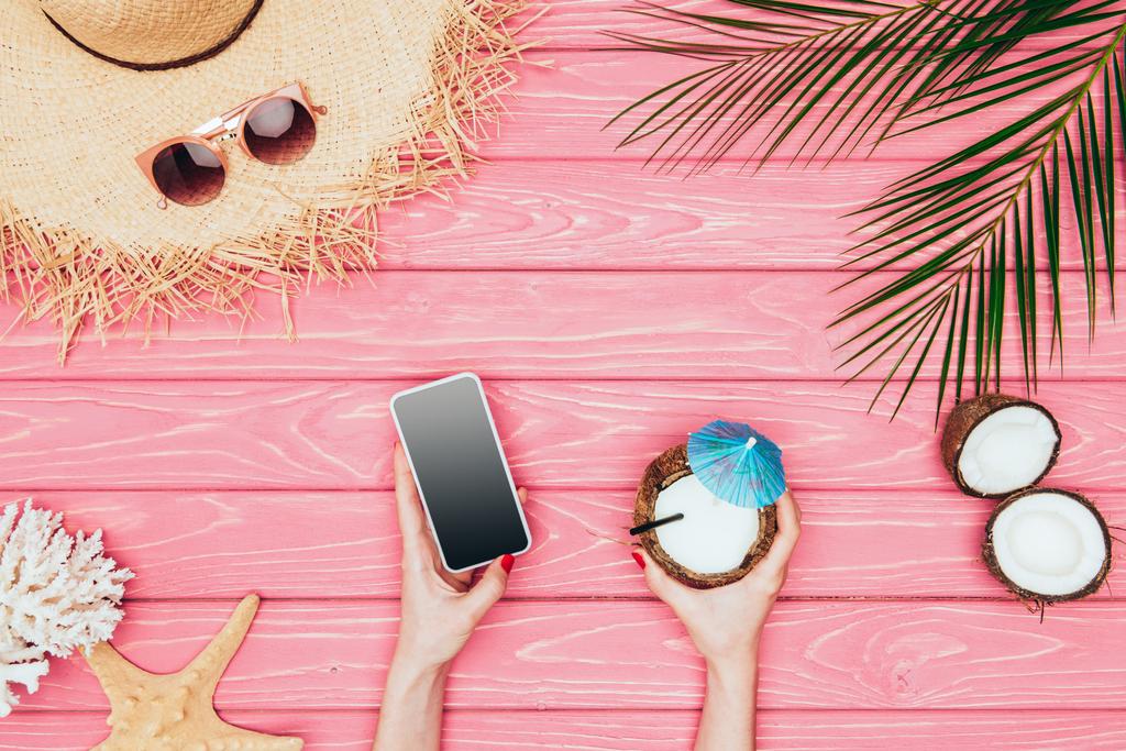 przycięty Zrzut z kobieta trzymając smartfon i kokos koktajl różowy powierzchni drewnianych - Zdjęcie, obraz