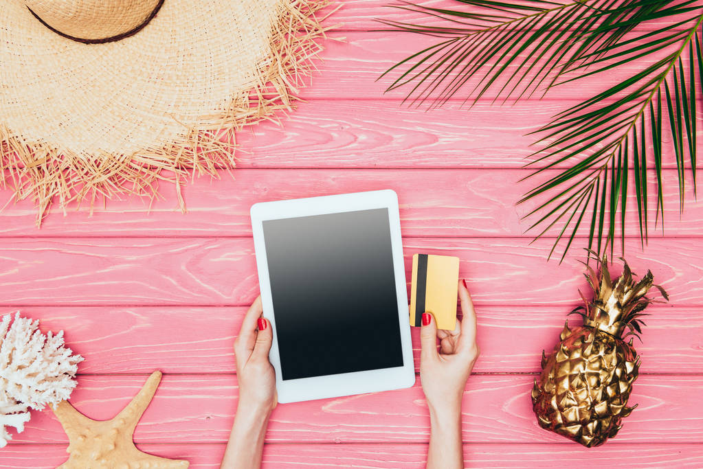 Schnappschuss einer Frau mit digitalem Tablet und Kreditkarte auf rosa Holzoberfläche mit goldener Ananas  - Foto, Bild