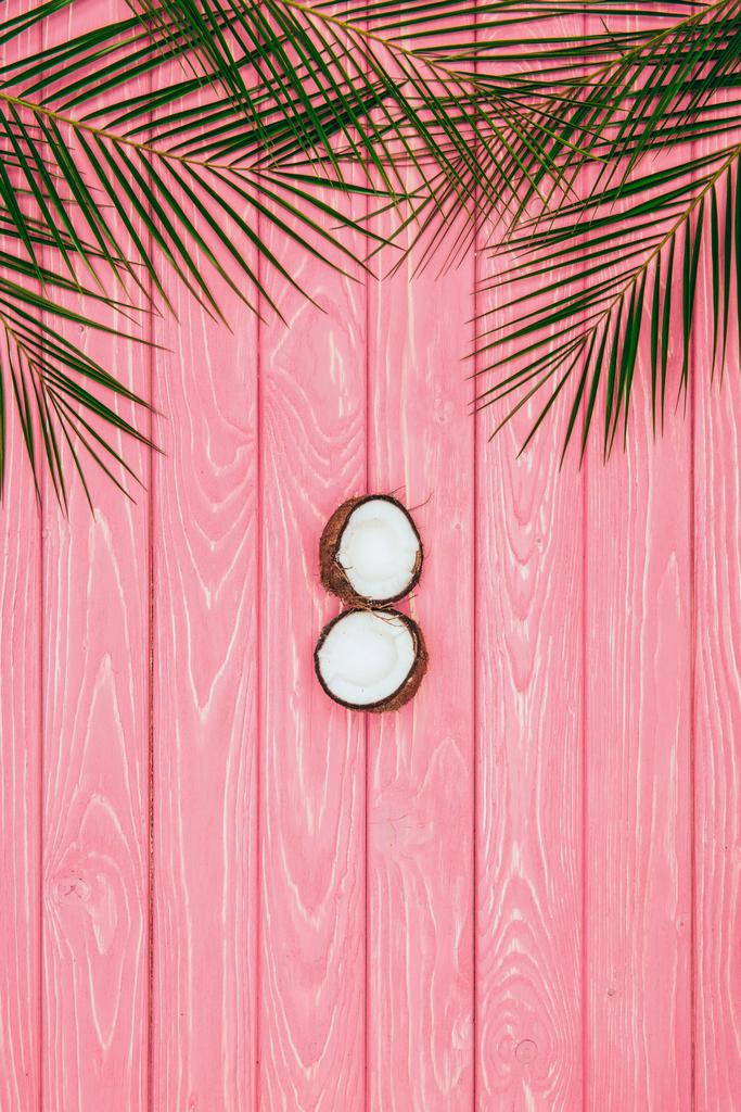 top view of halved coconut and palm leaves on pink wooden surface - Photo, Image