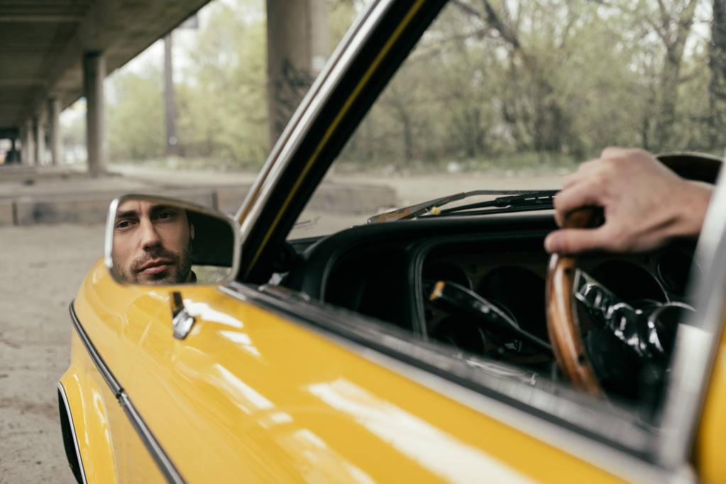 обрізаний знімок бородатого чоловіка, відображений у дзеркалі жовтого класичного автомобіля
 - Фото, зображення