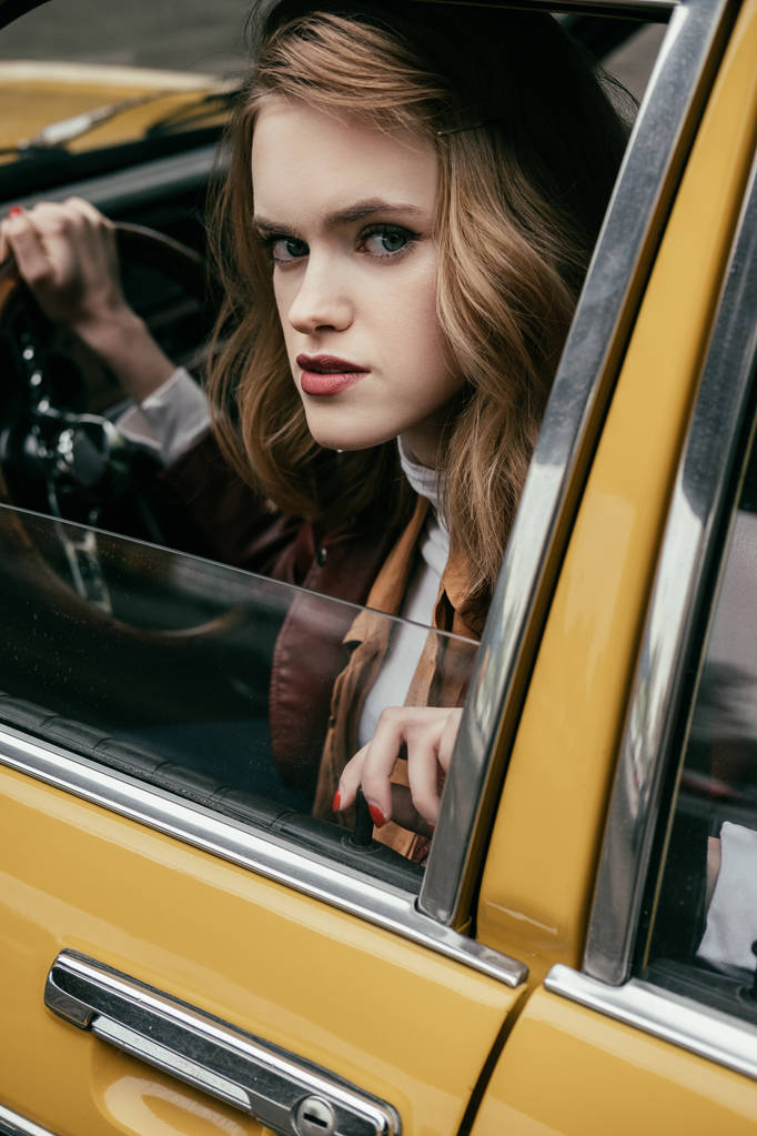 Крупный план девушки, смотрящей на камеру, сидя в классическом автомобиле
 - Фото, изображение