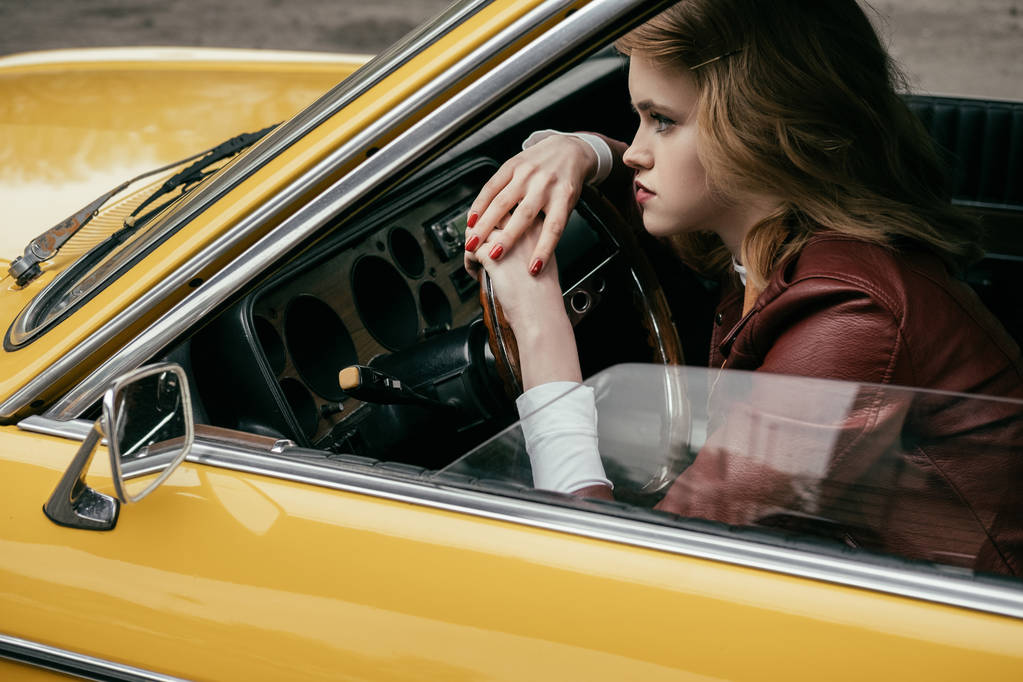 schöne Mädchen lehnt am Lenkrad und schaut weg, während sie in gelbem Auto sitzt  - Foto, Bild