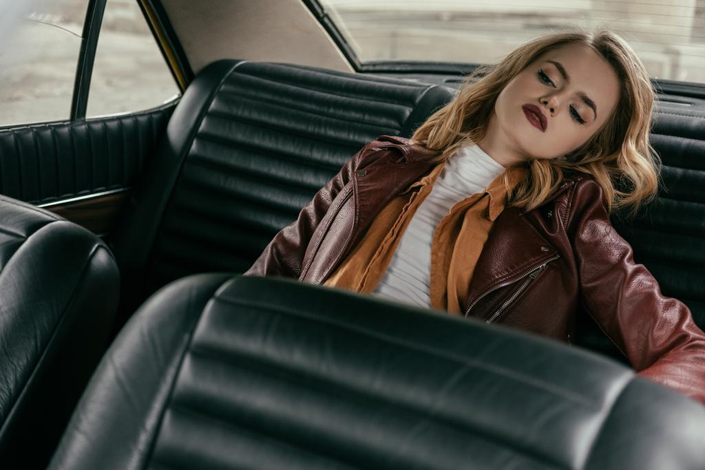 όμορφη αισθησιακό κορίτσι με δερμάτινο μπουφάν, κάθεται στο αυτοκίνητο και αναζητούν μακριά - Φωτογραφία, εικόνα