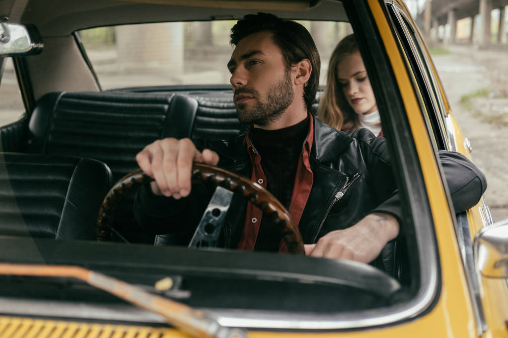 knappe jongeman rijden retro auto en vriendin zitten achter - Foto, afbeelding