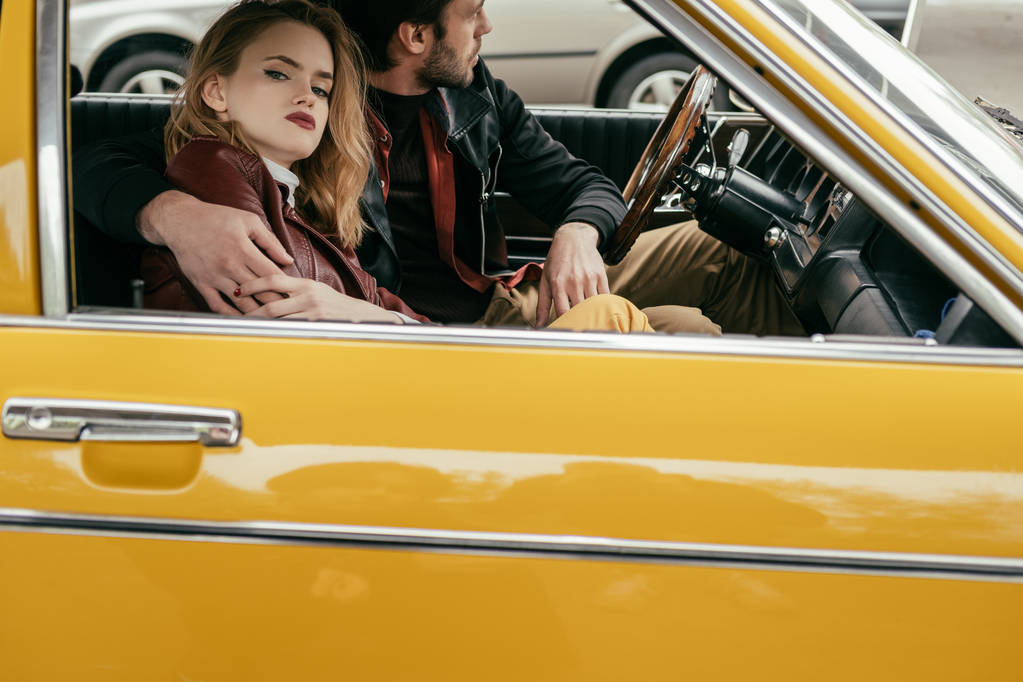 黄色のレトロな車で一緒に座ってスタイリッシュな若いカップルのショットをトリミング - 写真・画像