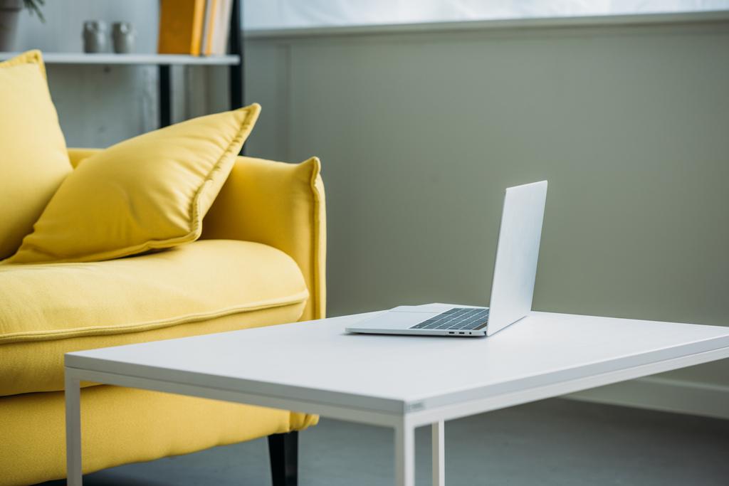 Laptop auf Tisch neben gelbem Sofa im Wohnzimmer - Foto, Bild