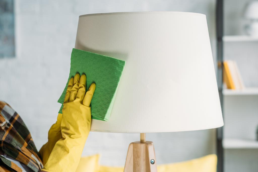 przycięty obraz kobiety odkurzanie lampy szmatą w domu - Zdjęcie, obraz