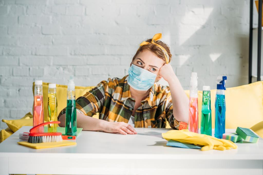beautiful tired woman sitting at table with cleaning supplies at home - Photo, Image