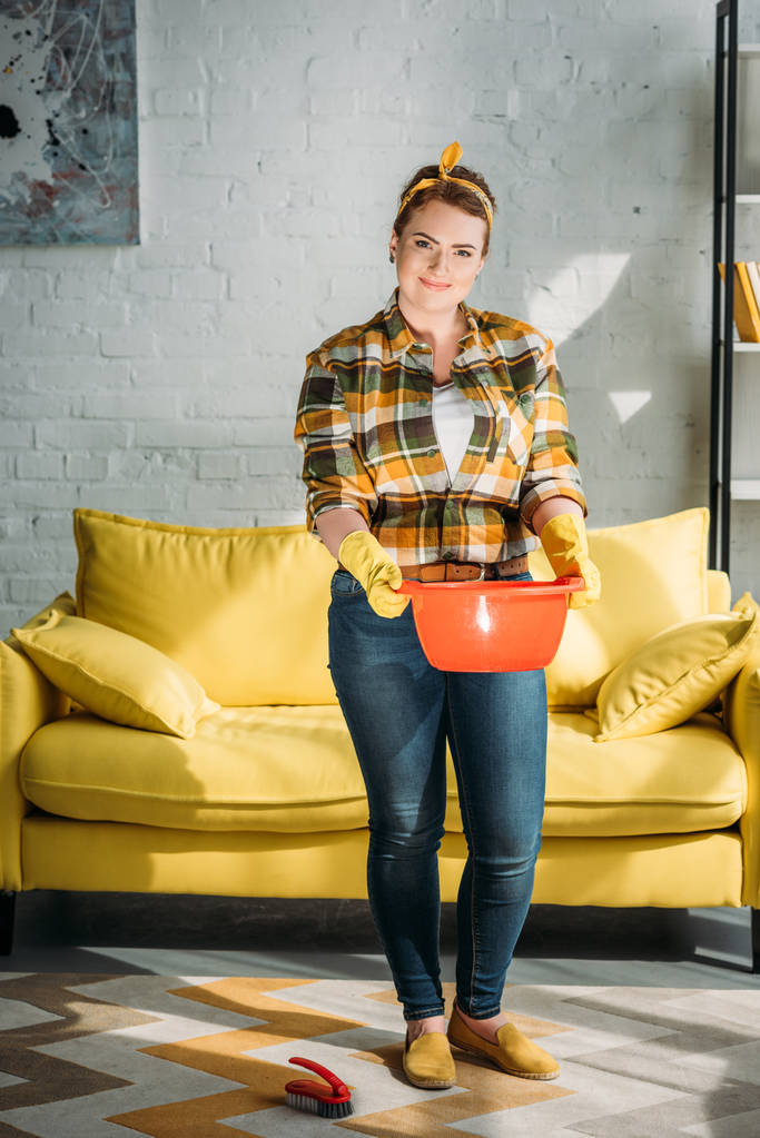 atractiva mujer sosteniendo cubo rojo con agua para limpiar en casa
 - Foto, Imagen