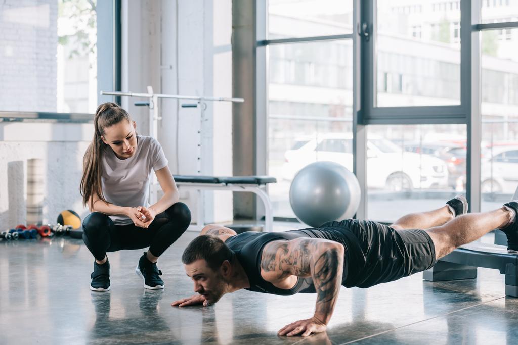 female personal trainer looking at sportsman doing push ups at gym - Photo, Image