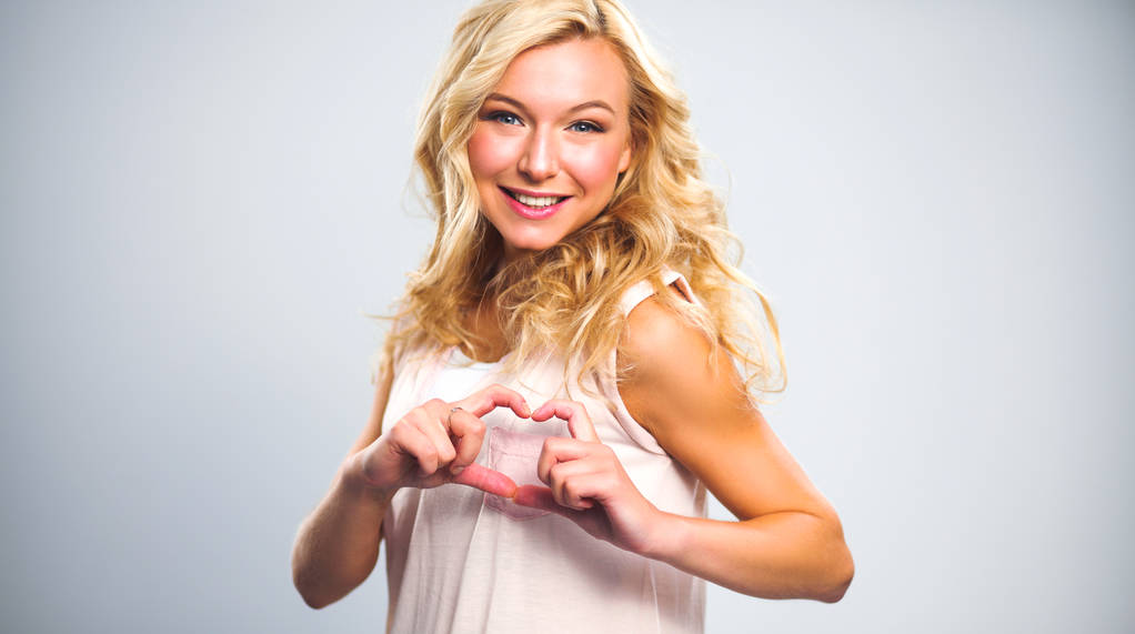Menina sorridente em camisas brancas mostrando coração com as mãos
 - Foto, Imagem