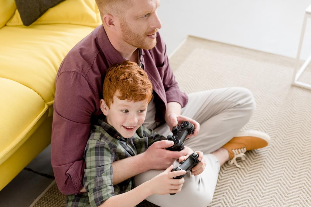 korkea kulma näkymä onnellinen isä ja poika leikkii joysticks kotona
 - Valokuva, kuva