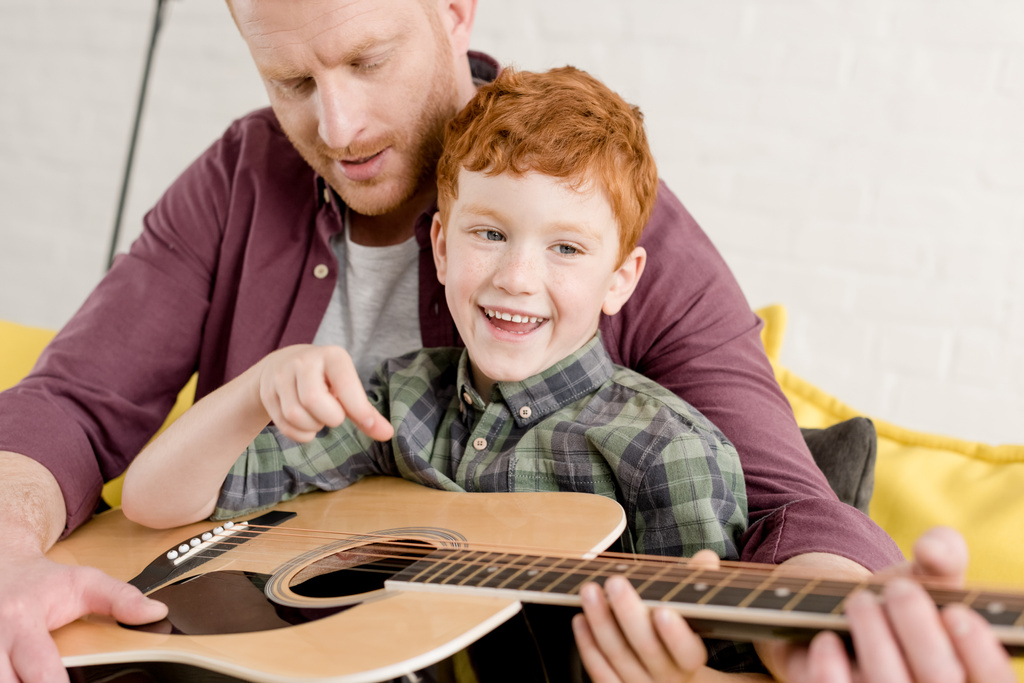 περικοπεί shot του πατέρα διδασκαλία χαρούμενος ο γιος παίζει κιθάρα στο σπίτι - Φωτογραφία, εικόνα