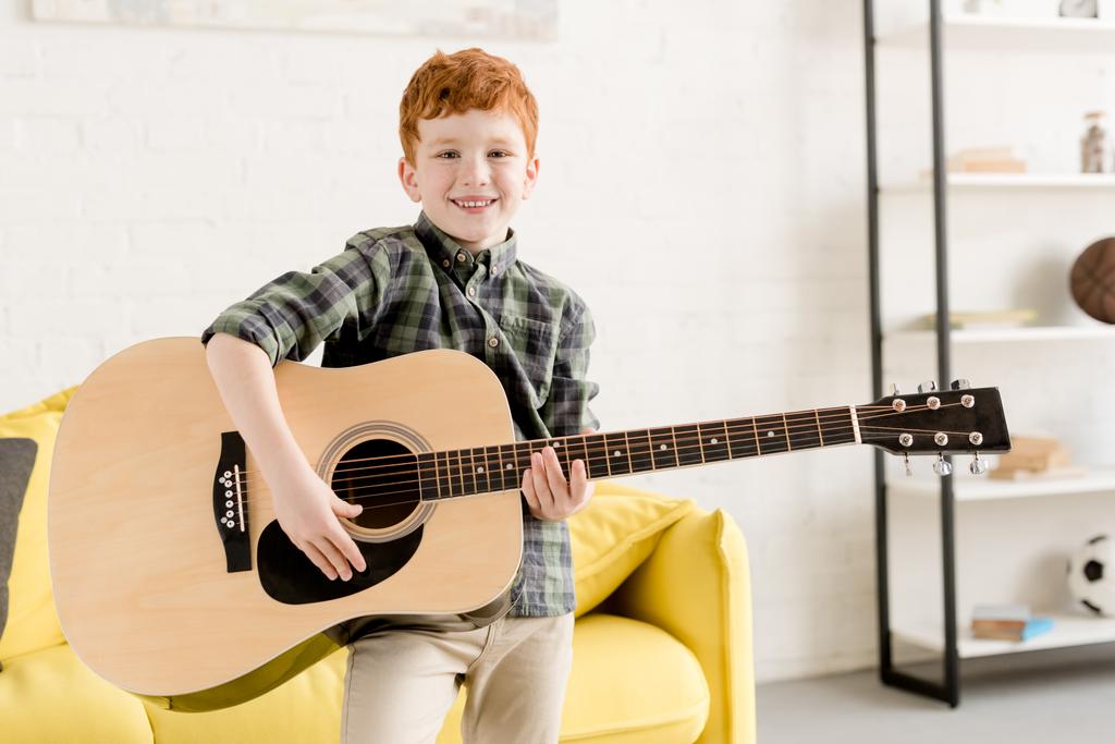 schattige kleine jongen holding akoestische gitaar en glimlachend op camera - Foto, afbeelding