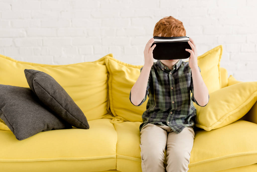 милий маленький хлопчик у гарнітурі віртуальної реальності сидить на дивані
 - Фото, зображення