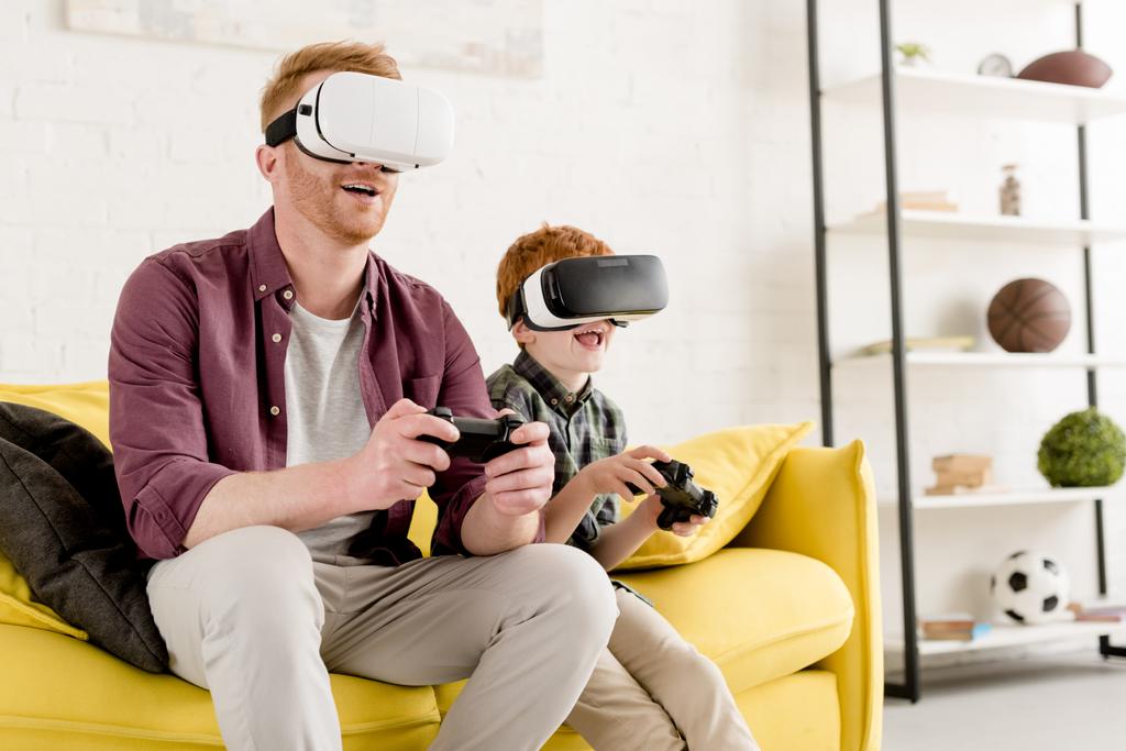 gelukkig vader en zoon in virtual reality headsets spelen met joysticks thuis - Foto, afbeelding