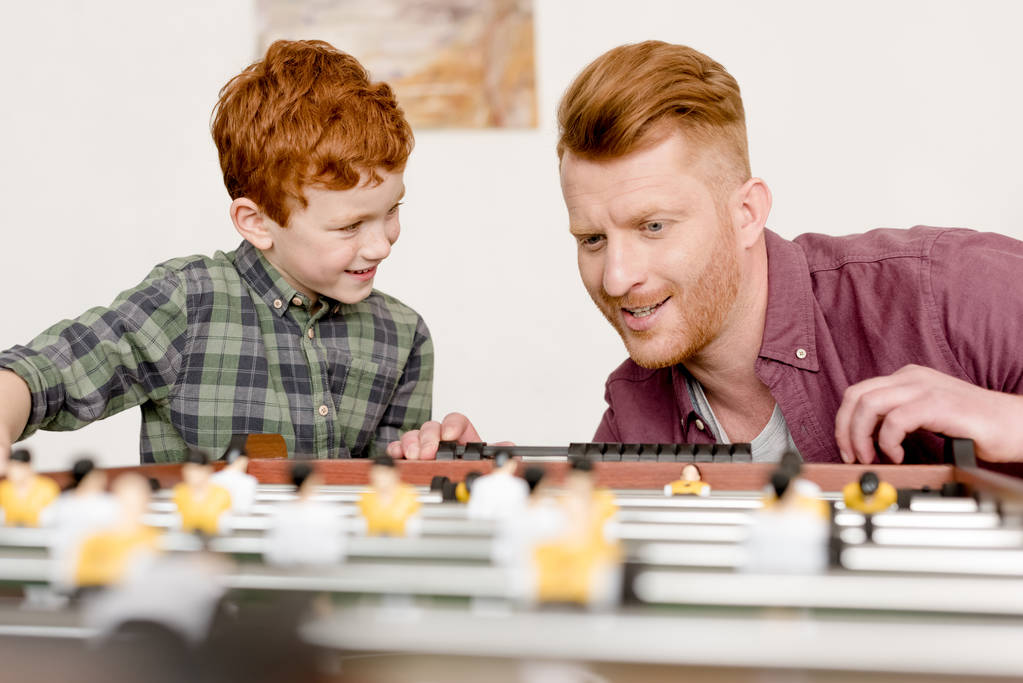 ευτυχισμένος/η κοκκινομάλλης/α πατέρας και γιος παίζοντας επιτραπέζιο ποδόσφαιρο μαζί στο σπίτι   - Φωτογραφία, εικόνα