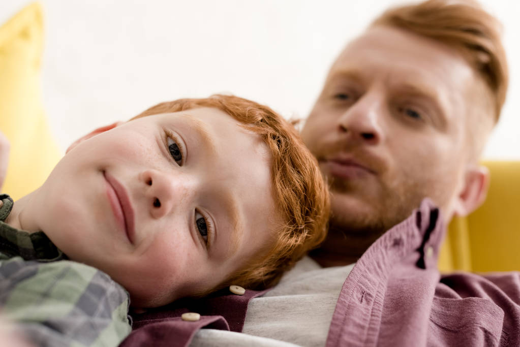 Detailní pohled milý chlapeček se usmívá na kameru při trávení času s otcem doma - Fotografie, Obrázek