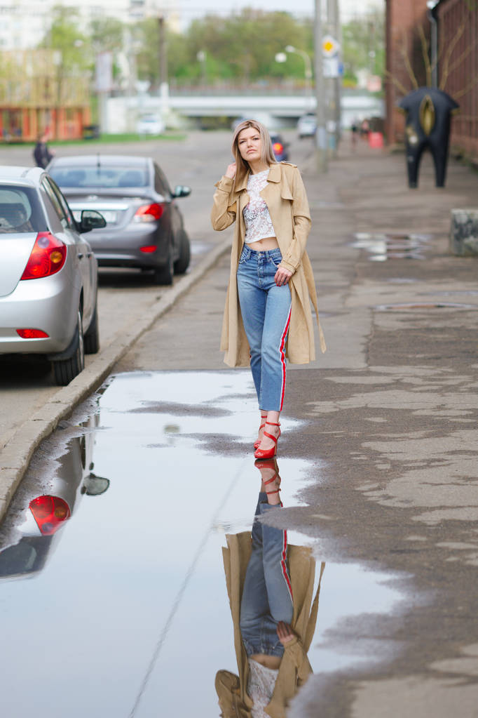 Bella ragazza in jeans corti e impermeabile che cammina per strada dopo la pioggia
 - Foto, immagini