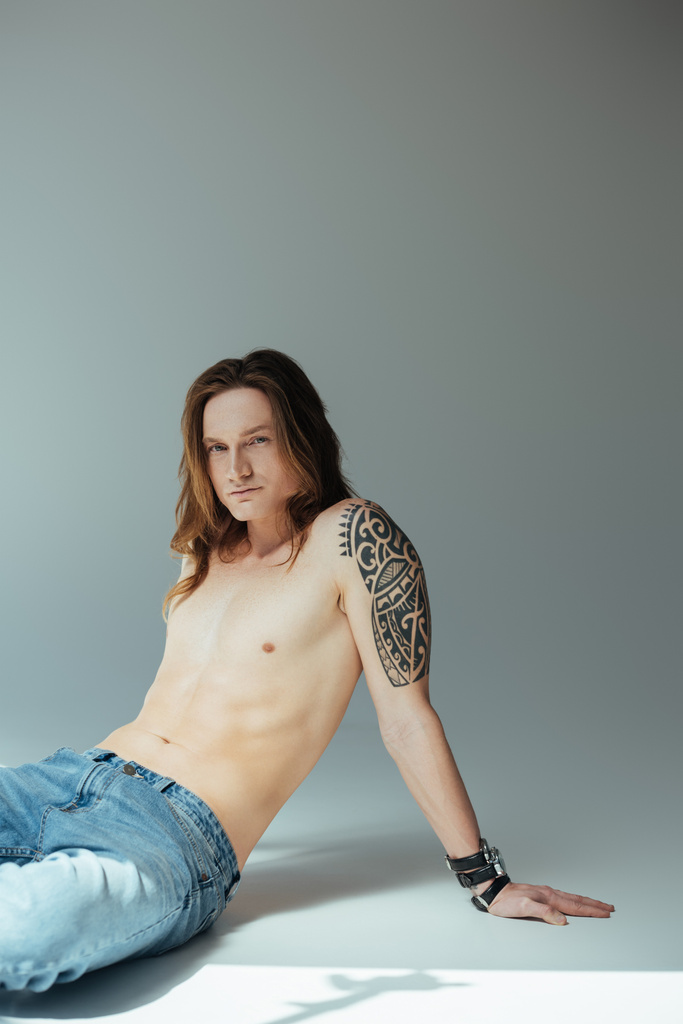 sexy getatoeëerd shirtless man poseren voor mode-shoot, op grijs - Foto, afbeelding
