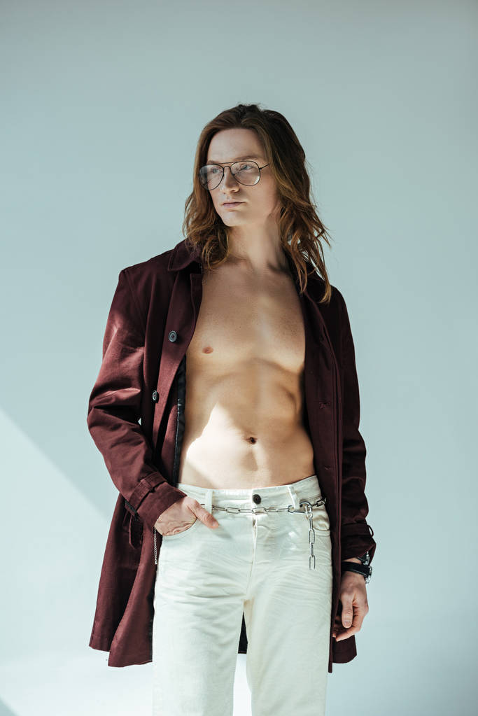 fashionable shirtless man in glasses posing in trench coat, on grey - Photo, Image