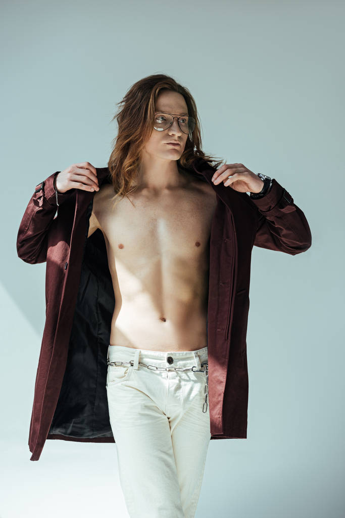 modieuze shirtless man poseren in trenchcoat, op grijs - Foto, afbeelding