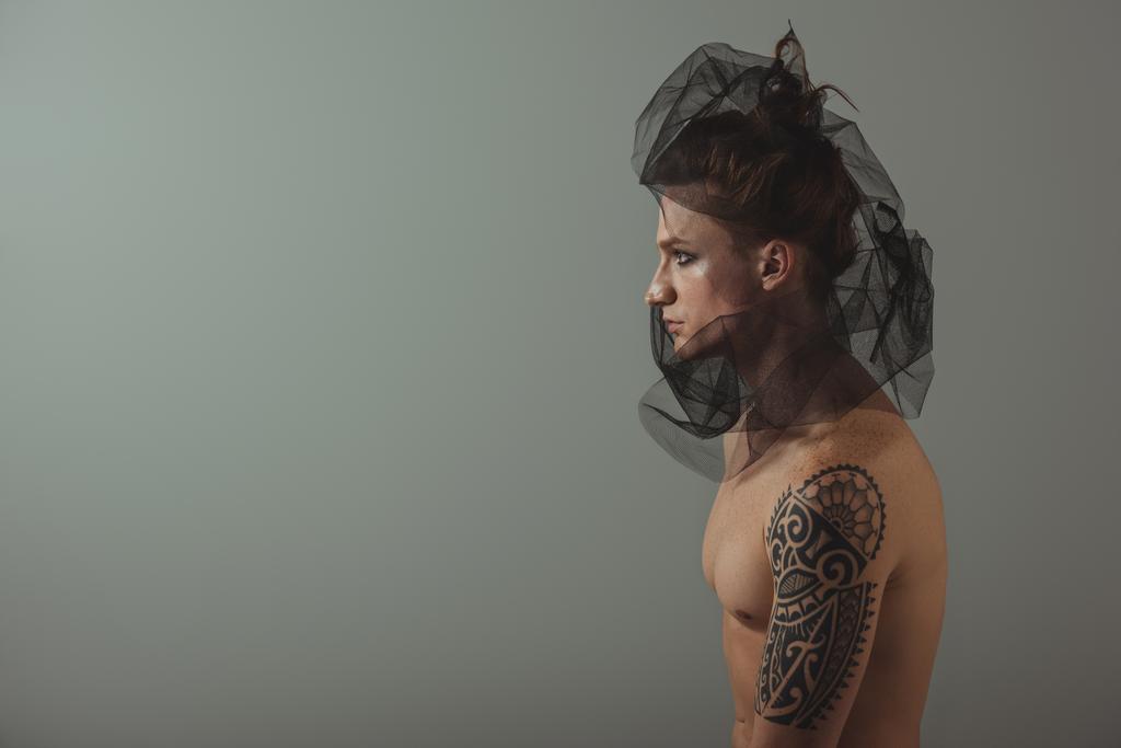 безрубашечный татуированный мужчина позирует с черной сеткой на голове для модной съемки, изолированный на сером
 - Фото, изображение