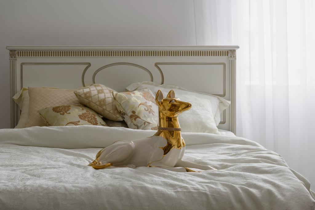 Kutya szobrocska ágyon fehér ágynemű a szobában - Fotó, kép