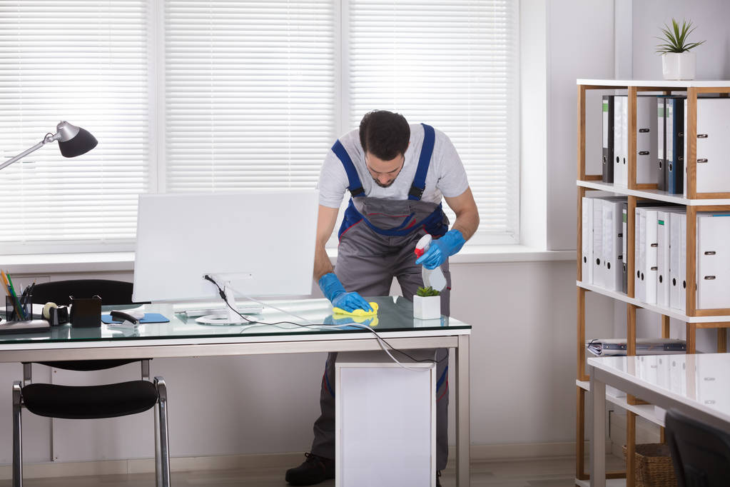 Nuori mies työntekijä käyttäen Spray puhdistus Office Desk
 - Valokuva, kuva