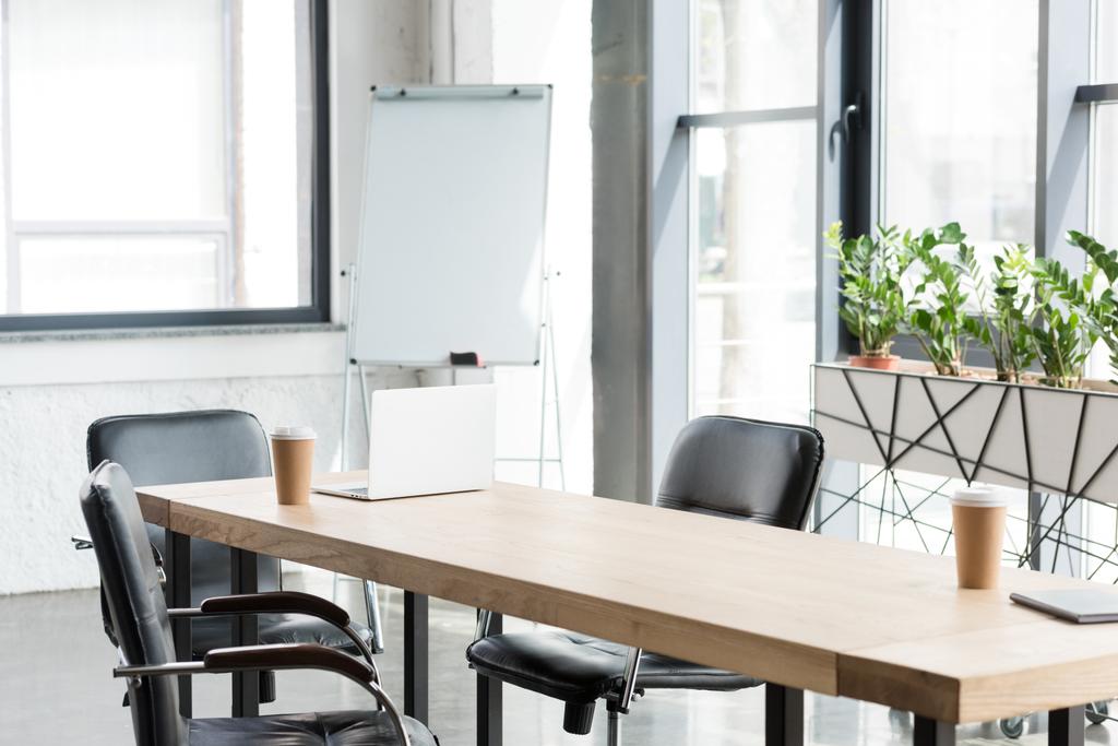wegwerp koffie kopjes en laptop op houten tafel in de moderne kantoor - Foto, afbeelding