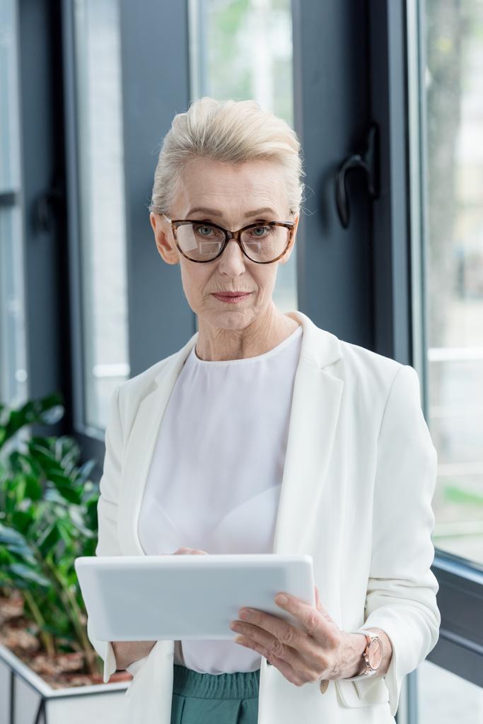 aantrekkelijke senior zakenvrouw in brillen houden digitale tablet en camera te kijken - Foto, afbeelding