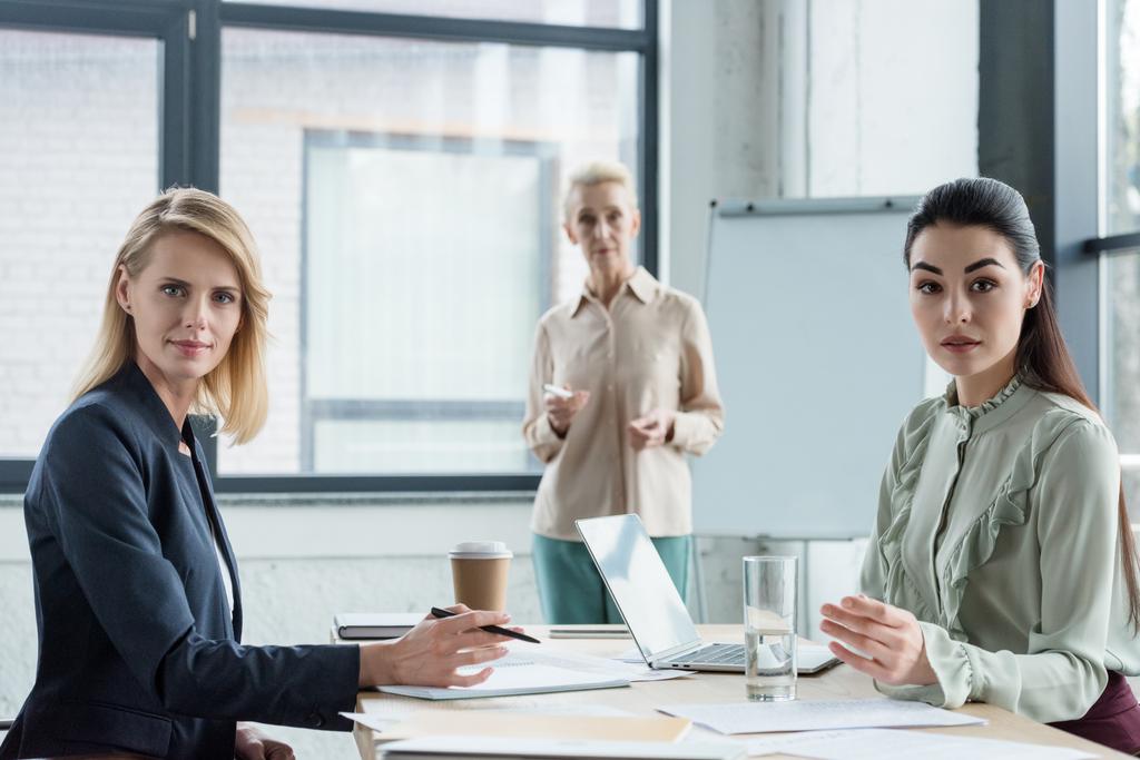 Berufstätige Geschäftsfrauen unterschiedlichen Alters blicken bei Treffen im Büro in die Kamera - Foto, Bild
