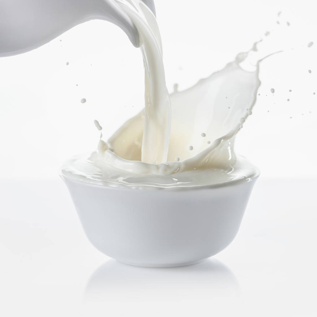 Gieten van melk van de kruik in kom op witte achtergrond - Foto, afbeelding