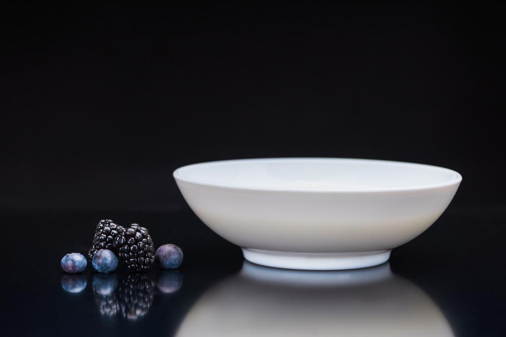 Mûres et bleuets par bol blanc sur fond noir
 - Photo, image