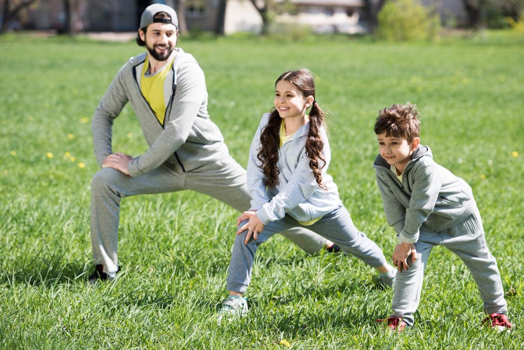 отец с дочерью и сыном занимаются физическими упражнениями на травянистом лугу в парке
 - Фото, изображение