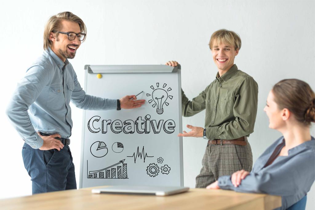 Smějící se podnikatelé zobrazující kreativní nápis a obchodní značky na flipchat podnikatelka - Fotografie, Obrázek