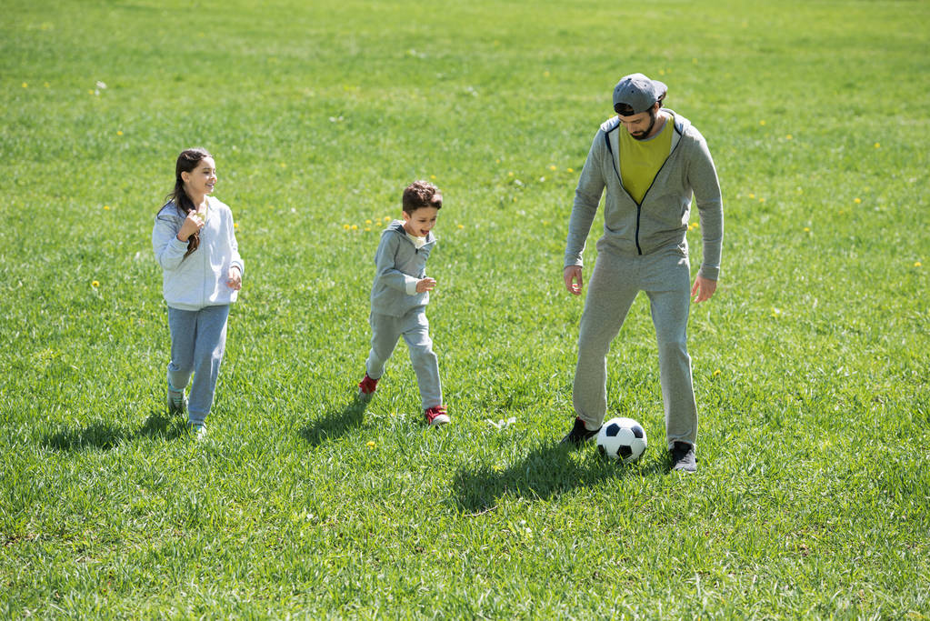 lapset pelaavat jalkapalloa isän kanssa puistossa
  - Valokuva, kuva