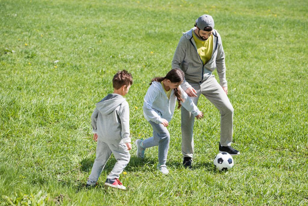 Улыбающийся отец играет в футбол с дочерью и сыном в парке
 - Фото, изображение