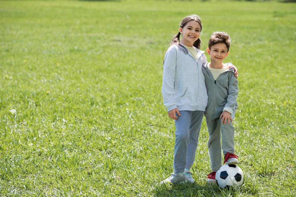 feliz hermano y hermana con bola de pie en prado herboso
  - Foto, imagen