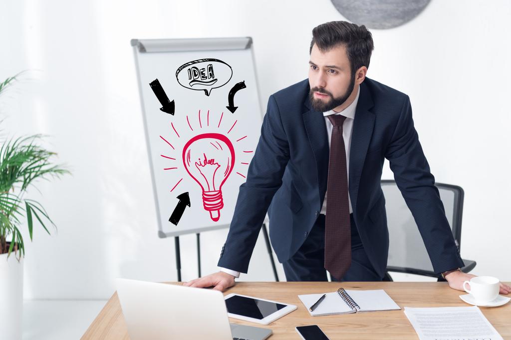 pensive businessman looking away at workplace in office with idea inscription and light bulb icon on whiteboard - Photo, Image