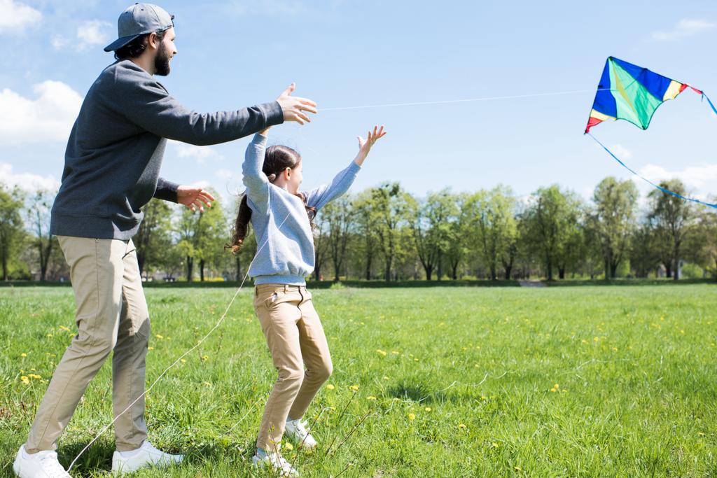 vista lateral da filha e pai voando pipa no prado
  - Foto, Imagem