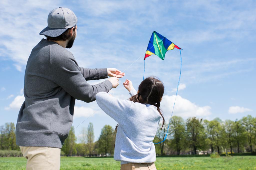 Achteraanzicht van vader en dochter vliegen vlieger op weide - Foto, afbeelding